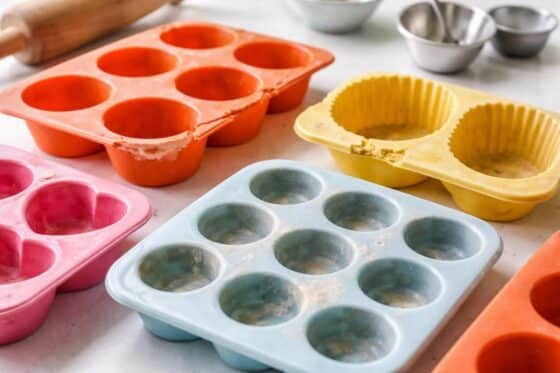 close-up of silicone molds showing tears, cracks, warping, and residue on a clean surface with baking tools nearby.
